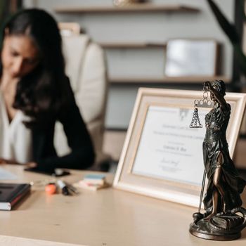 A woman is sitting at a desk with a statue of justice on it