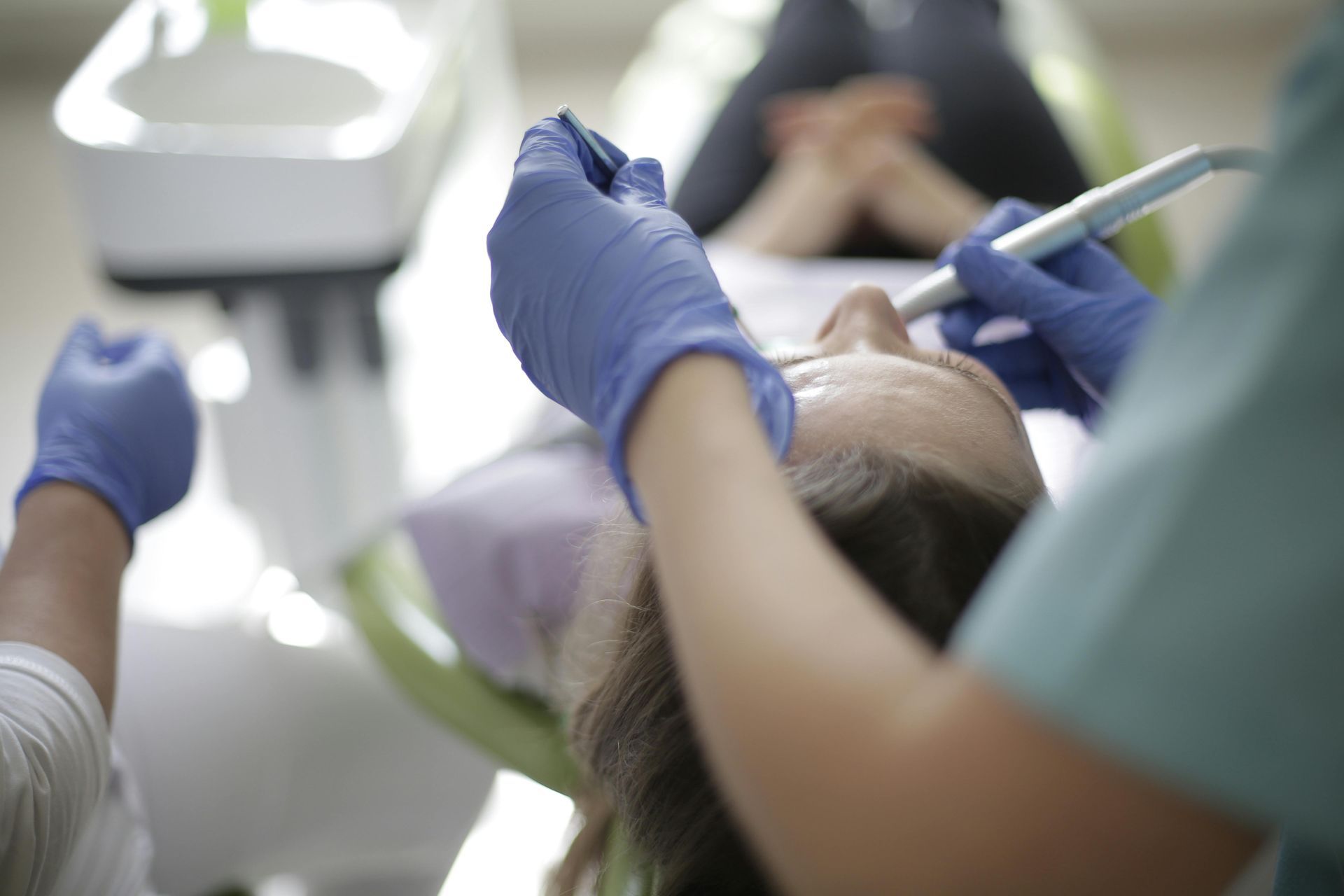 A person receiving dental work in a dentist's office. A dental professional wears blue gloves and leans over the patient.