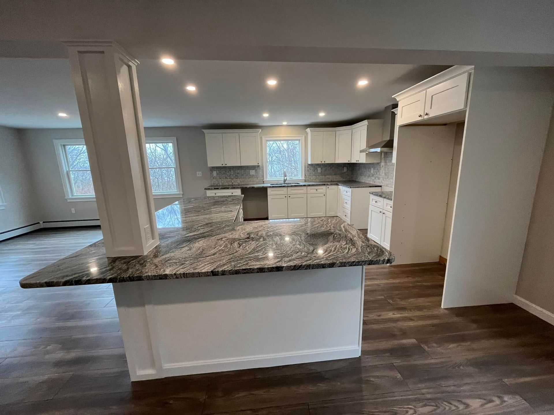 Modern kitchen with granite island, white cabinets, dark wood floors, and recessed ceiling lights.