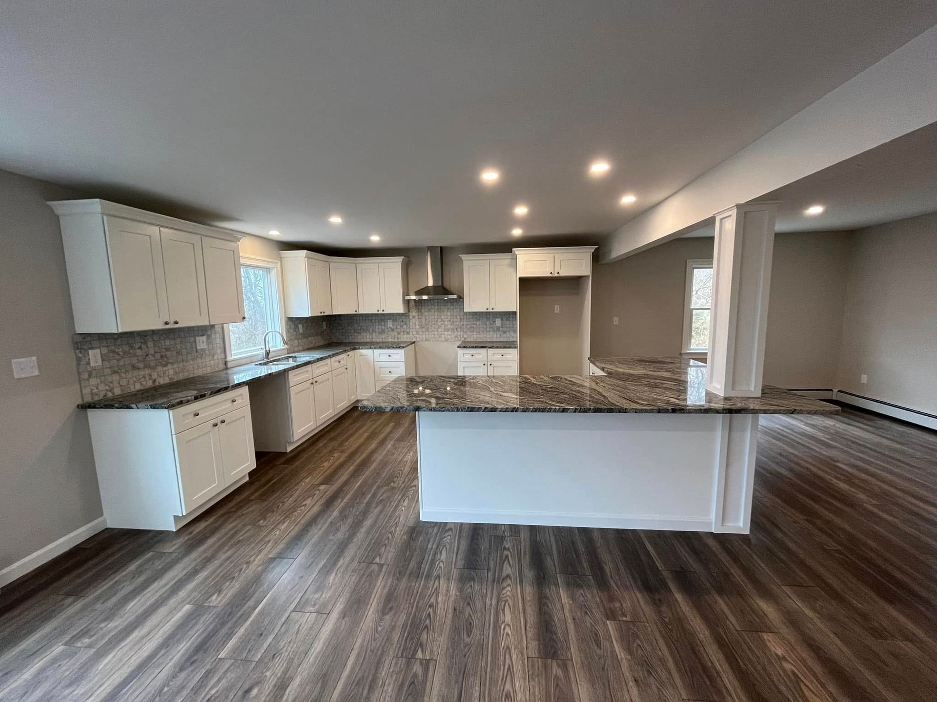 Spacious modern kitchen with white cabinets, granite island, and wood-look flooring
