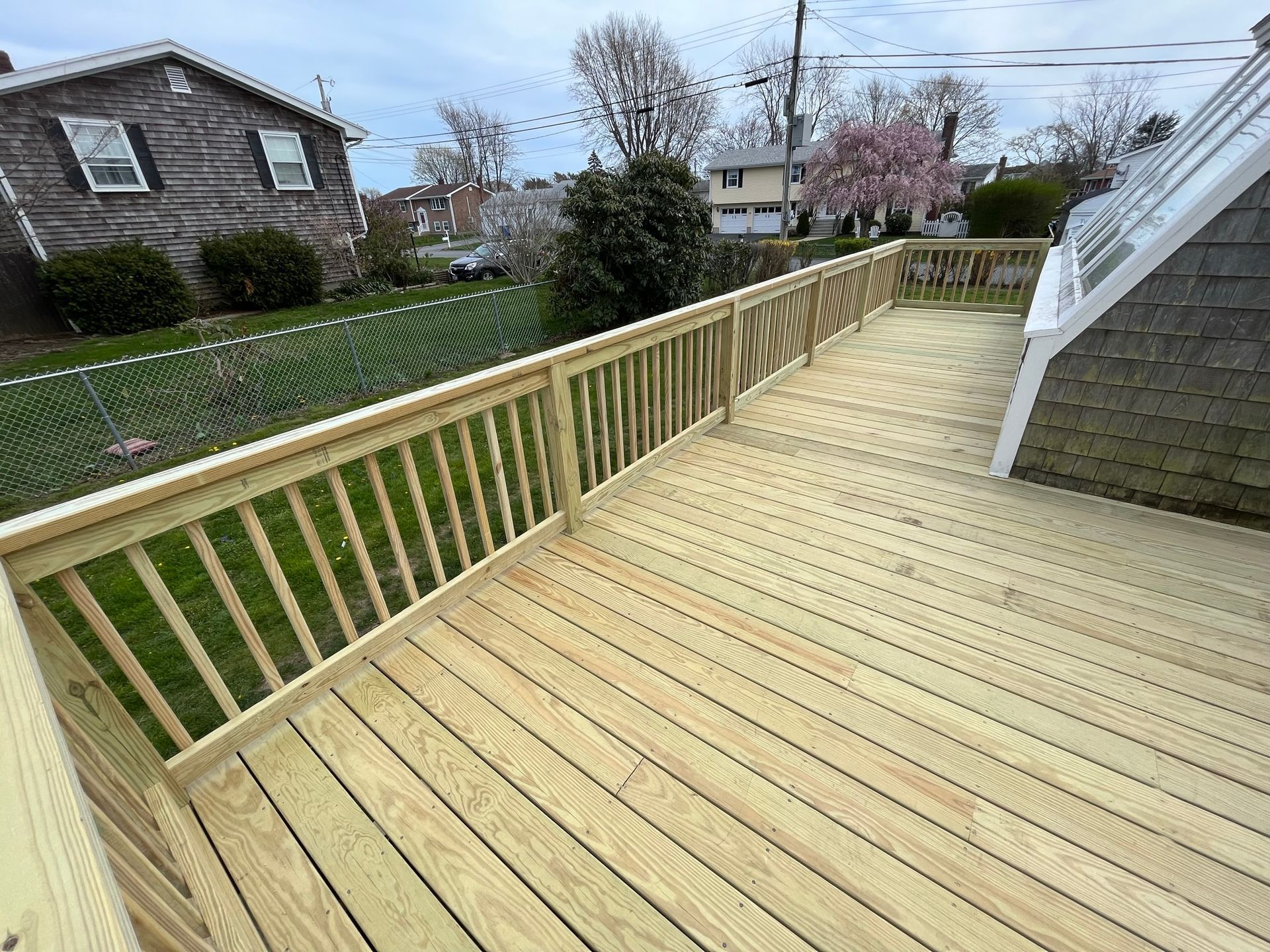 Wooden deck with railing overlooking a residential yard and neighboring houses on an overcast day