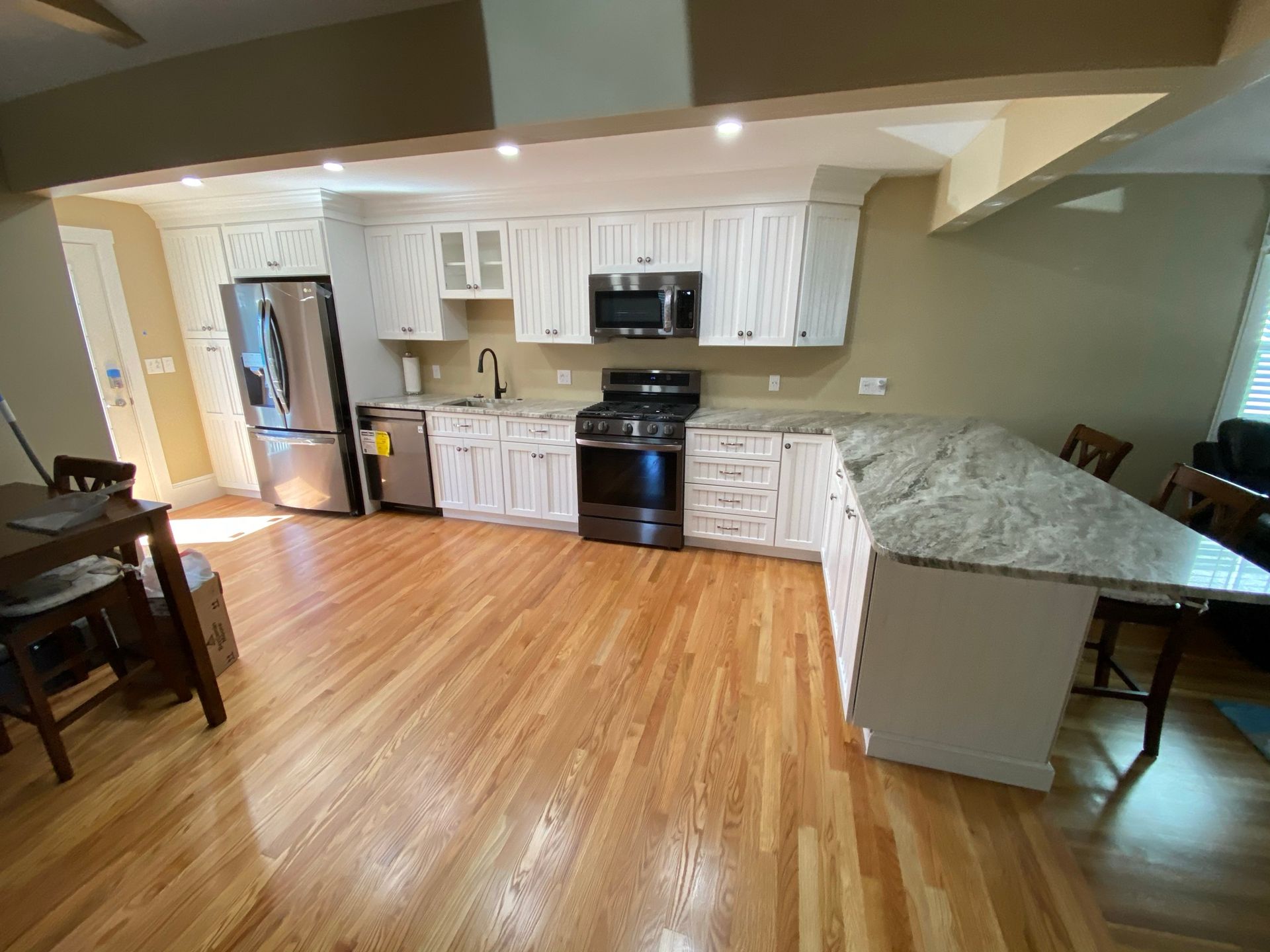 Open kitchen and dining area with white cabinets, stainless stove, granite island, and hardwood floors