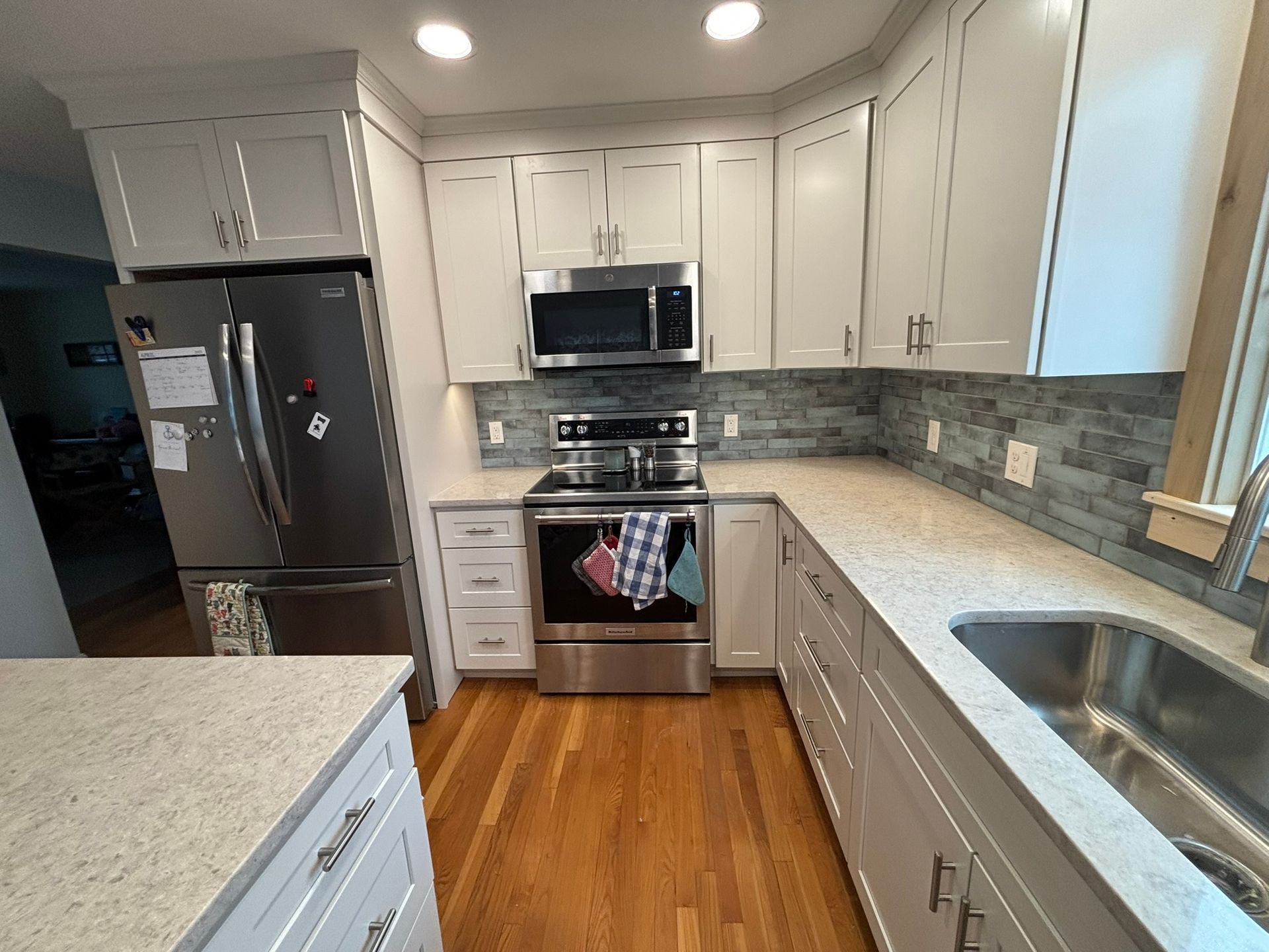 Bright modern kitchen with white cabinets, stainless appliances, gray tile backsplash, and wood floors