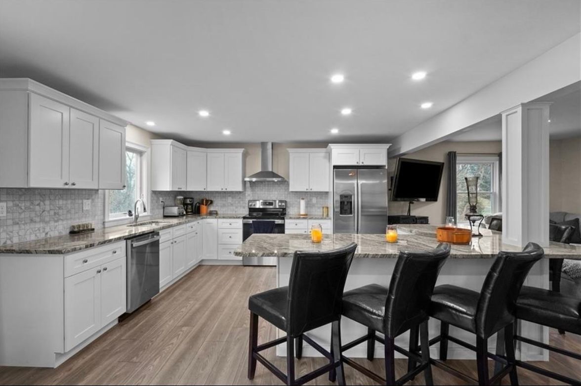 Modern white kitchen and dining area with black barstools, granite countertops, and stainless steel appliances
