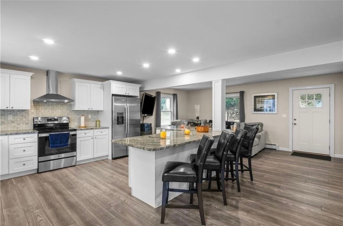 Modern kitchen with white cabinets, granite island, bar stools, stainless appliances, and wood-look flooring