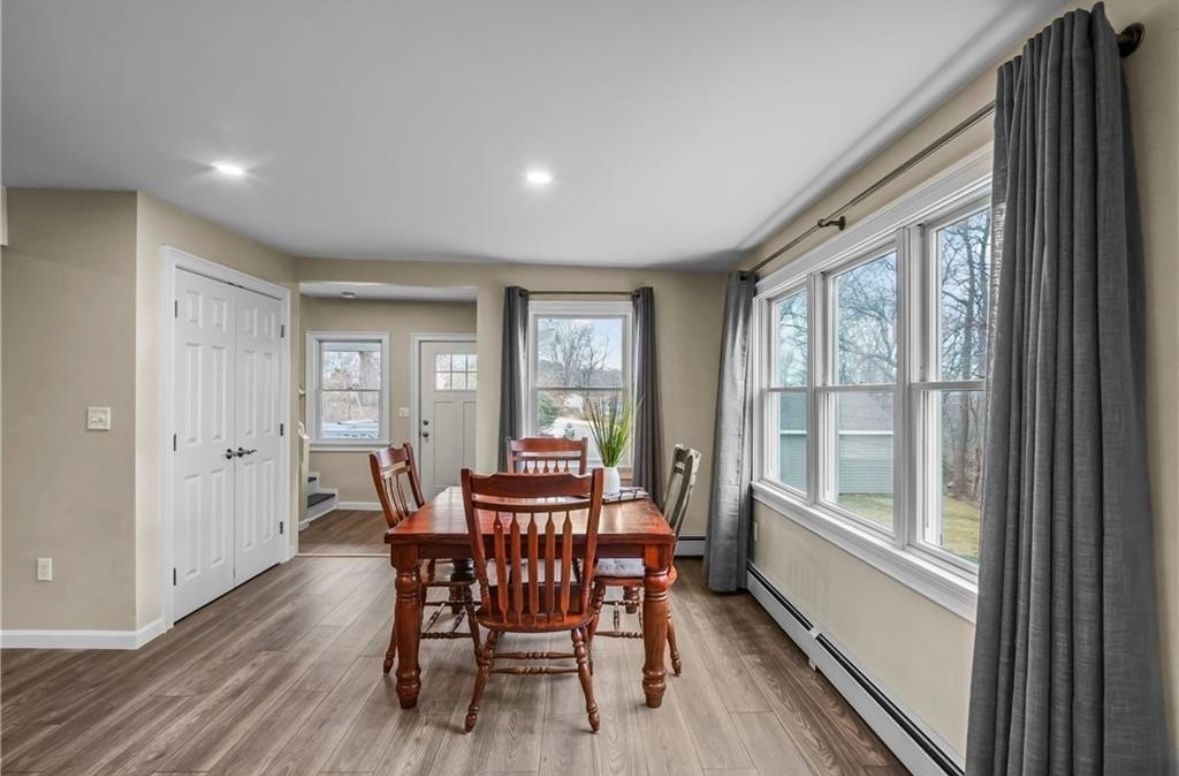 Dining room with wooden table and chairs, large windows, gray curtains, and light wood flooring.