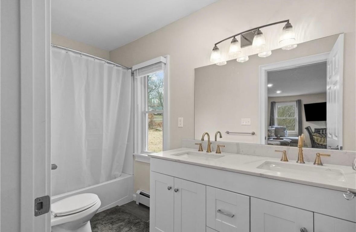 Modern bathroom with white vanity, large mirror, shower curtain, and window