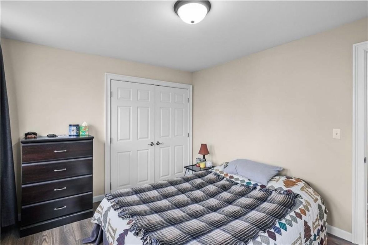 Small bedroom with a bed, dresser, and closed closet doors in beige walls.