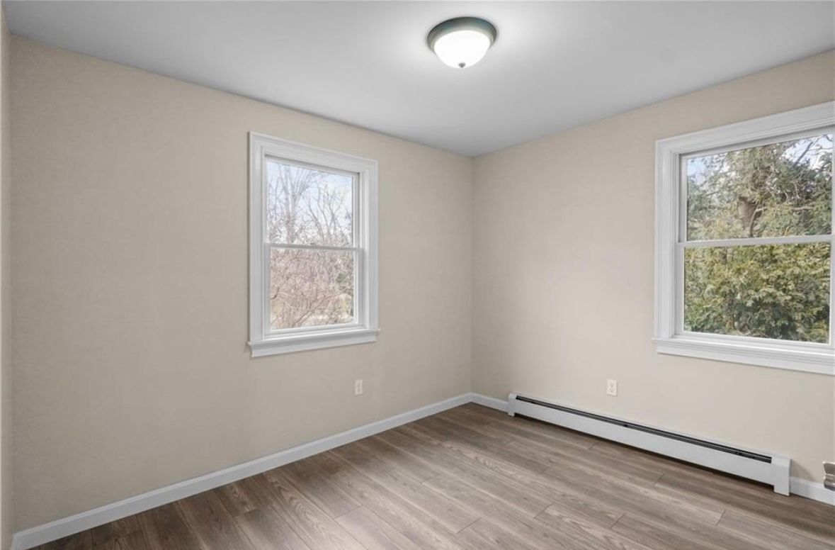 Empty beige room with two windows, wood-look flooring, and a ceiling light