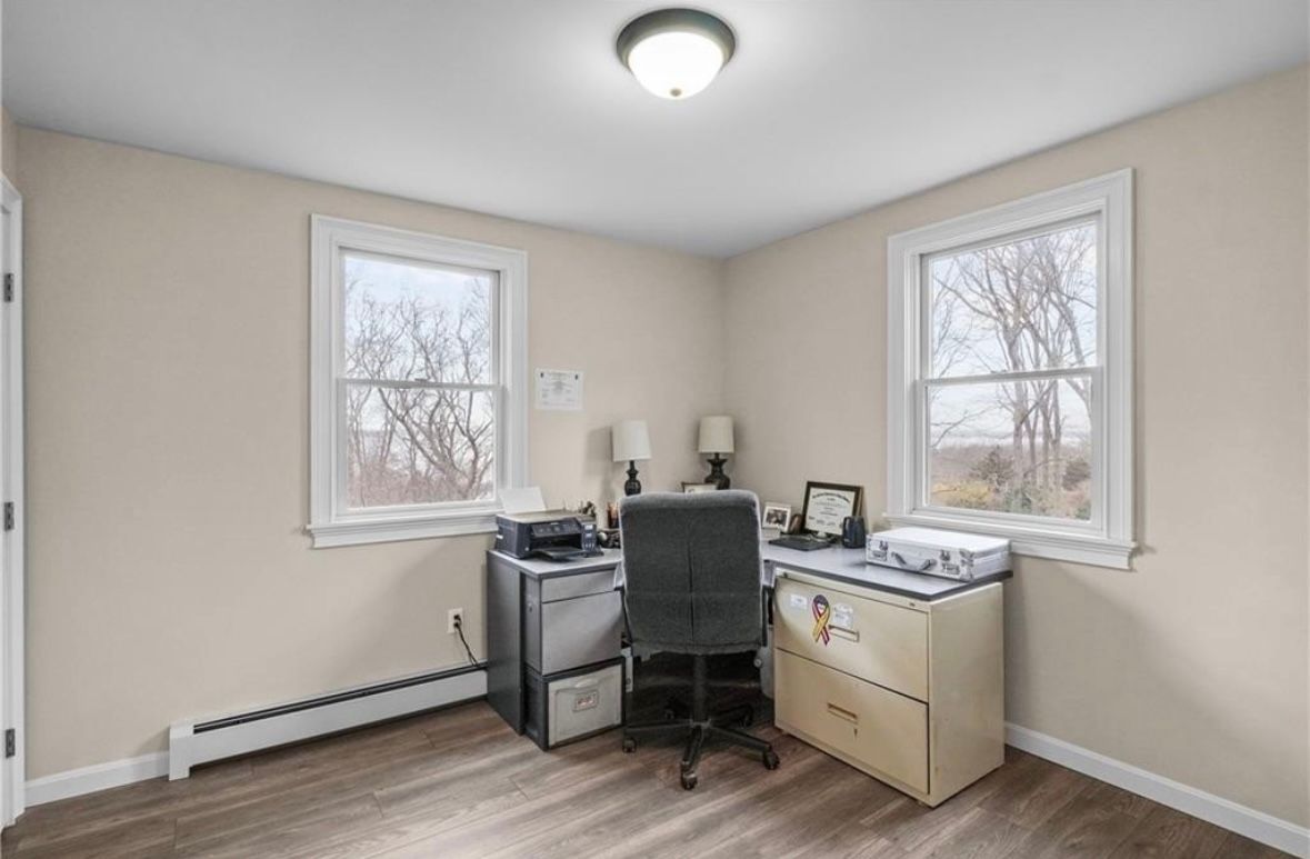 Small home office with desk, chair, printer, and two windows on beige walls.