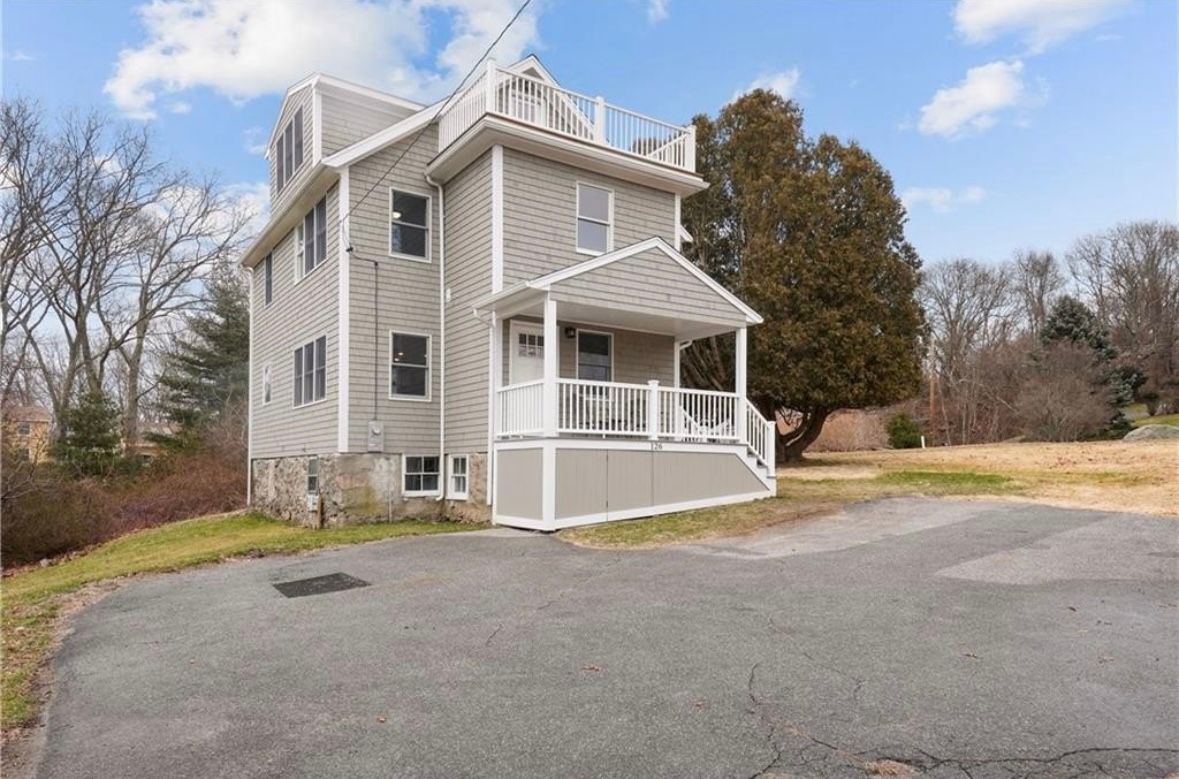 Gray two-story house with white porch on a gravel driveway under a partly cloudy sky