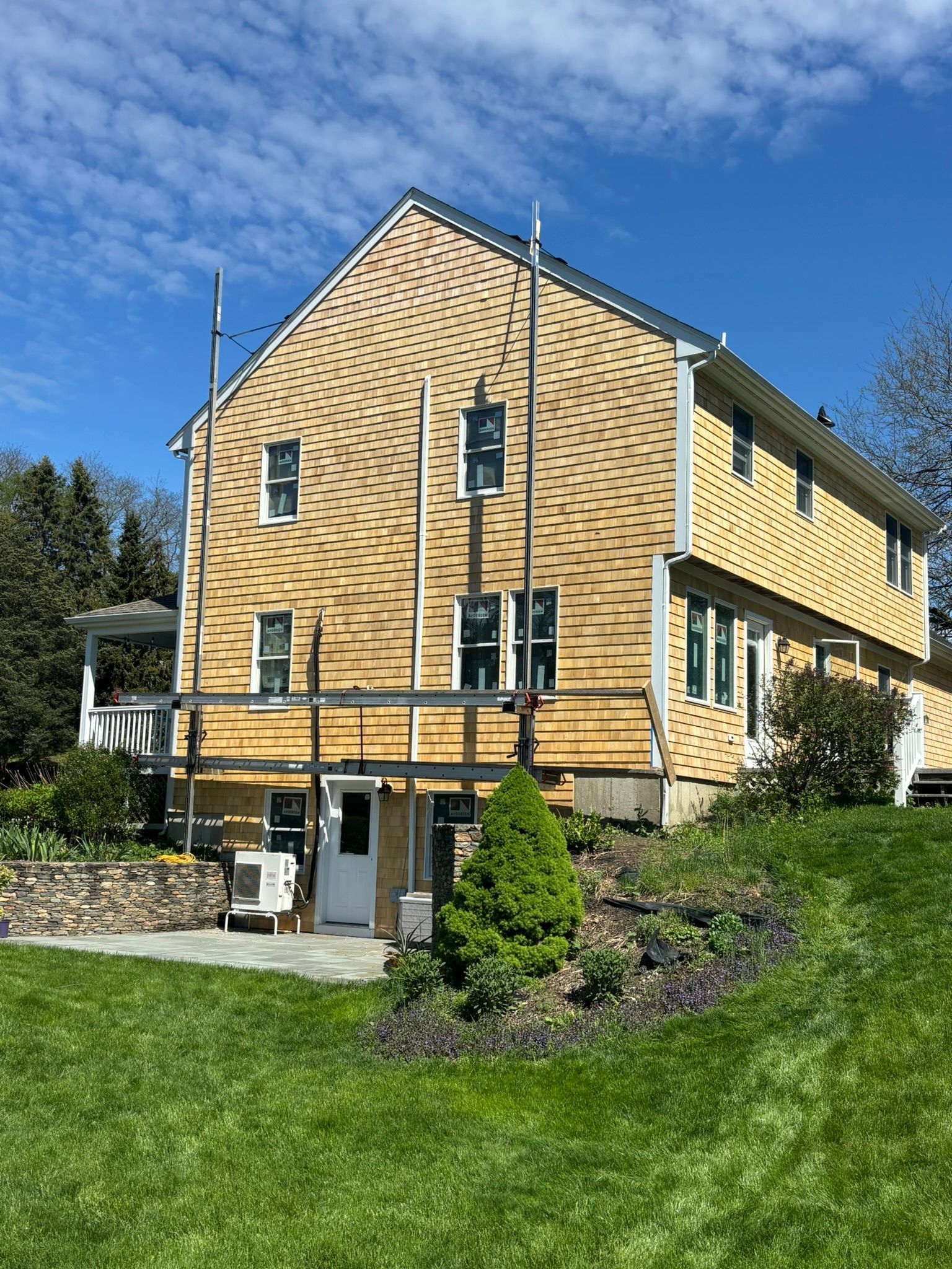 Yellow wooden house with steep roof on a grassy hillside under a clear blue sky