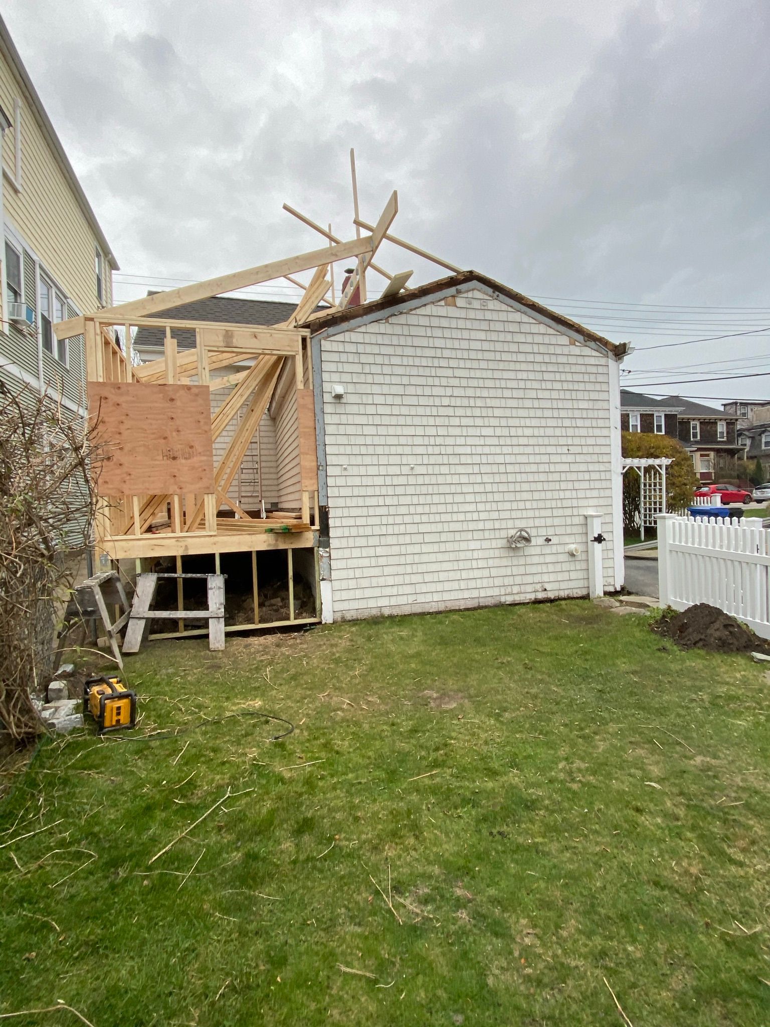 Partially demolished shed with exposed framing beside a house and grassy yard