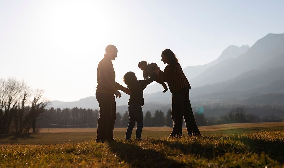 Familia en silueta jugando junta en un campo soleado con montañas al fondo.