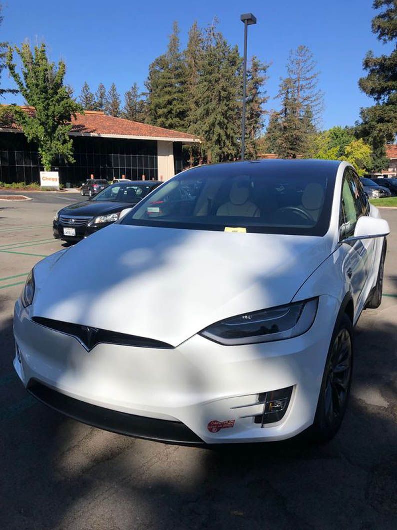 A white tesla model x is parked in a parking lot.