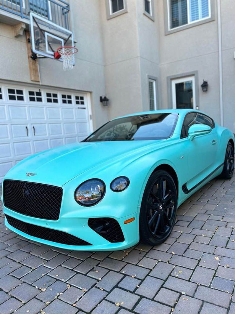 A mint green bentley is parked in front of a garage.