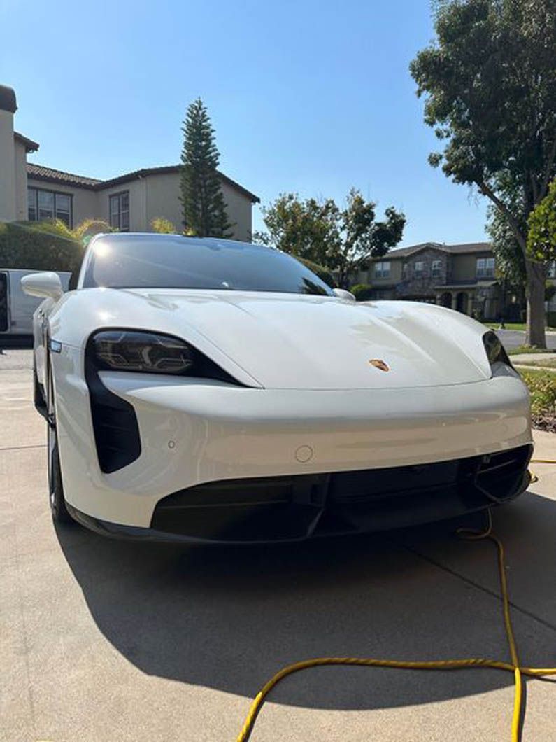 A white porsche taycan is parked in a driveway next to a house.