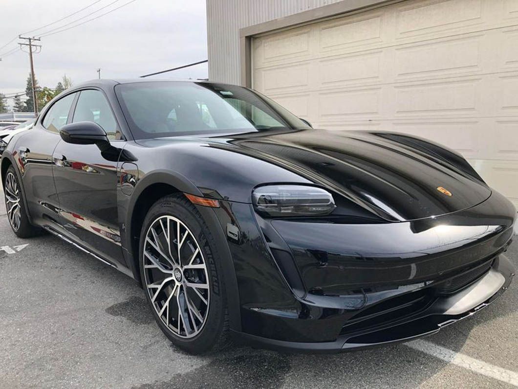 A black porsche taycan turbo s is parked in front of a garage.