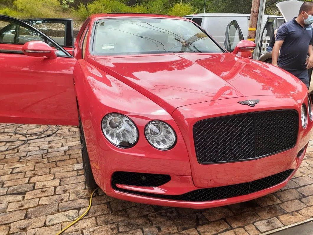 A red bentley is parked on a brick driveway with its doors open.