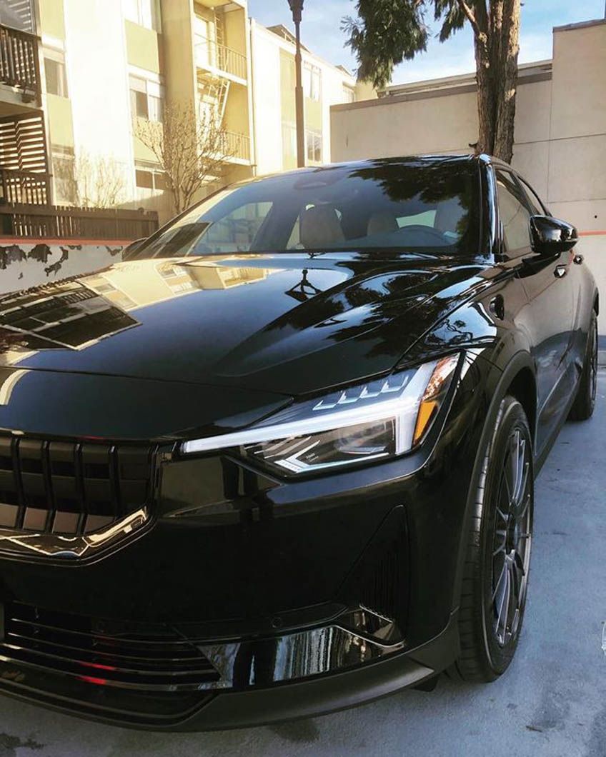 A black car is parked in a parking lot in front of a building.