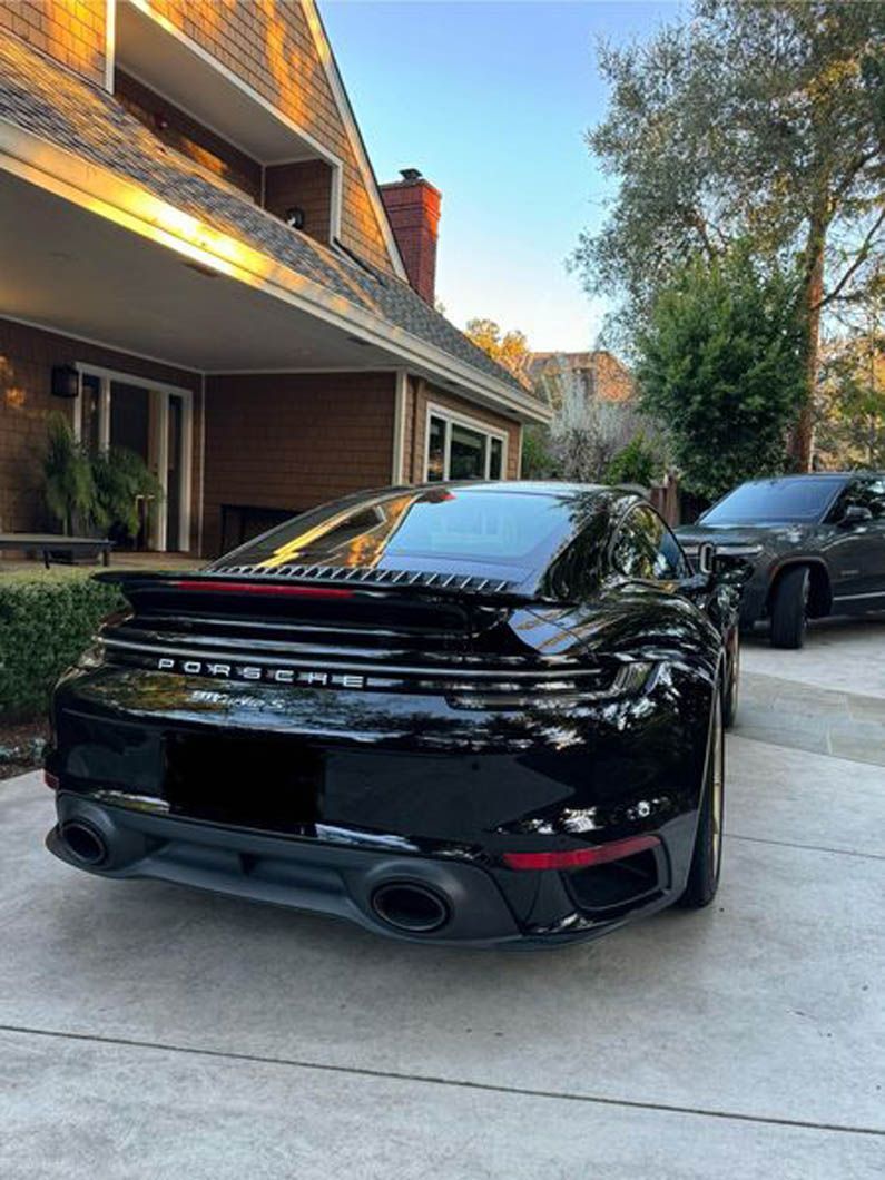 A black porsche turbo is parked in front of a house.