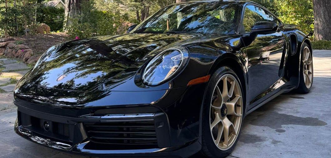 A black porsche 911 turbo s is parked in a driveway.