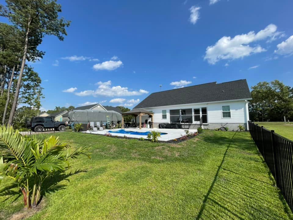 Backyard with pool, white house, and black fence on a sunny day.