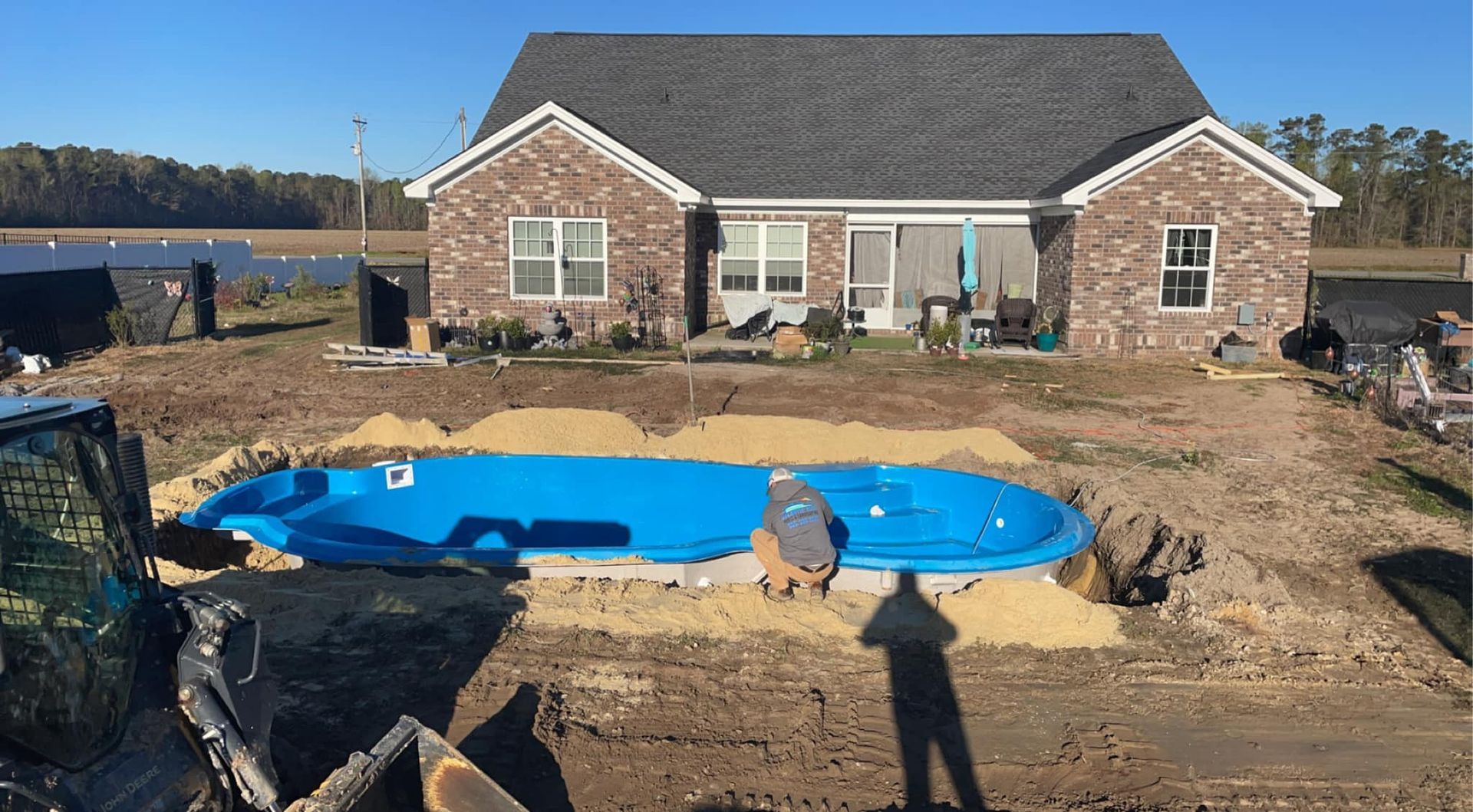 A blue pool being installed in a backyard. A house is in the background. Two people are working near the pool.