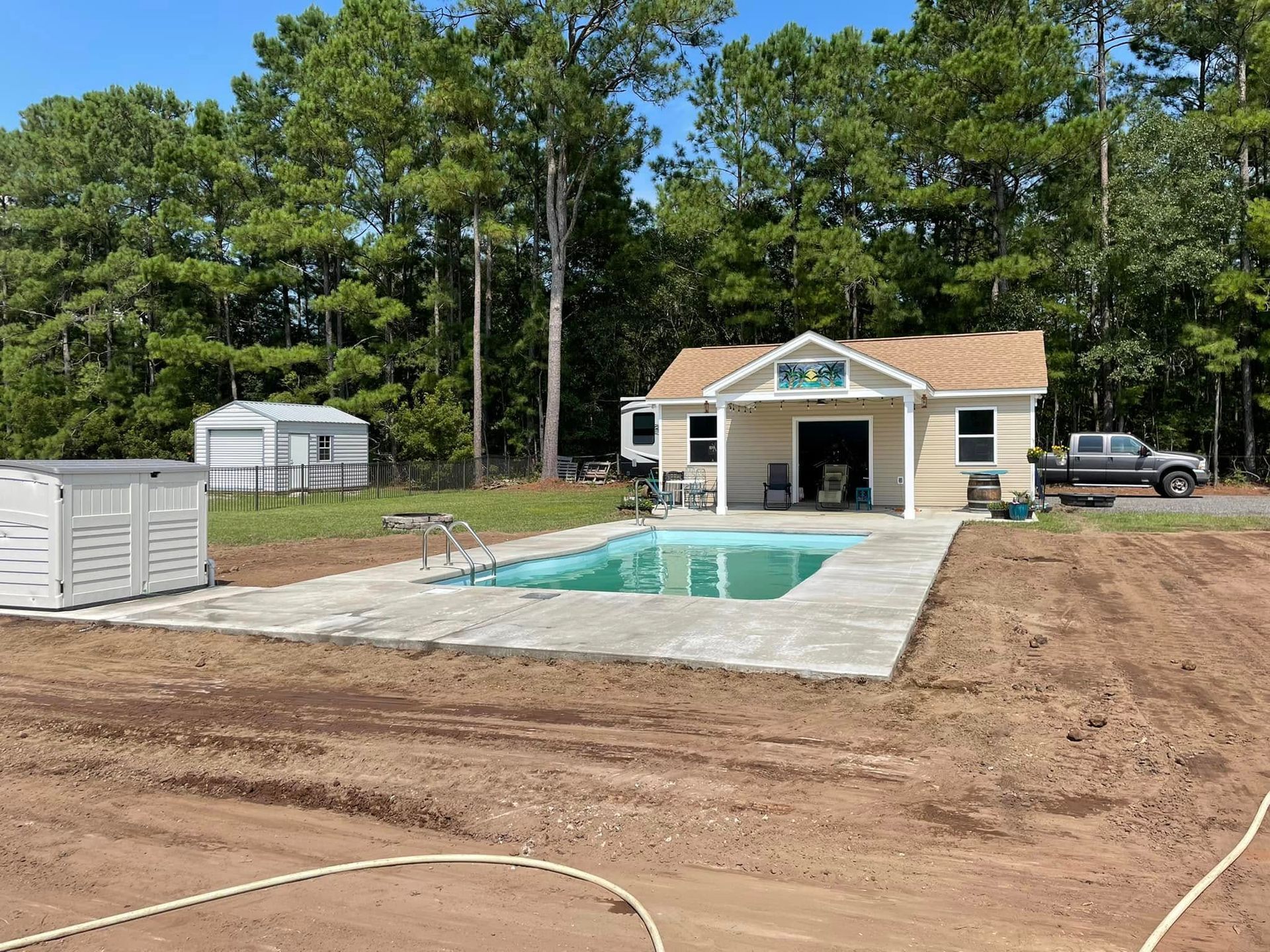 House with a pool and a shed in a wooded area. A truck is parked to the side.
