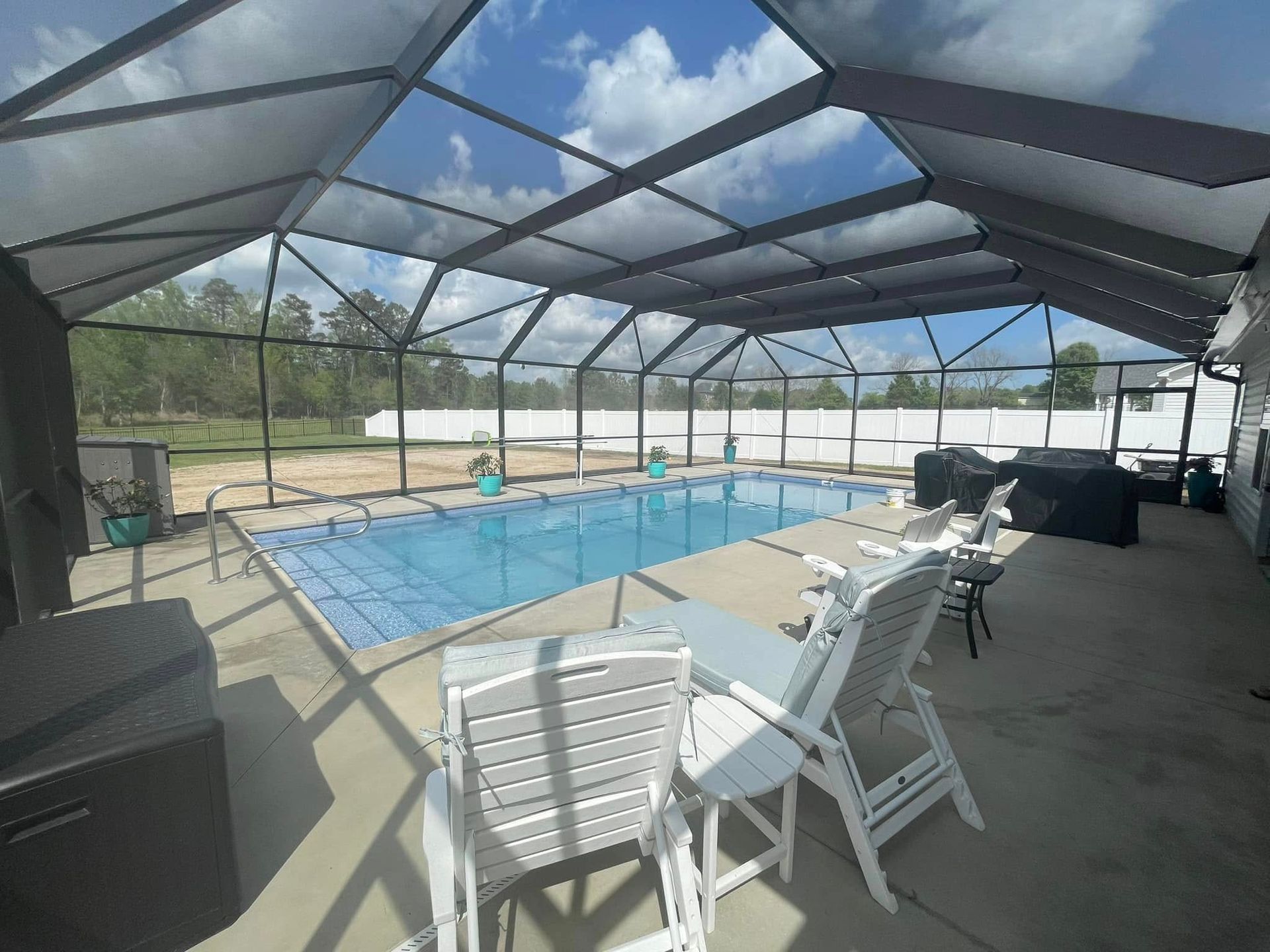 Pool enclosure with pool, chairs, and sky. Gray frame and white chairs.
