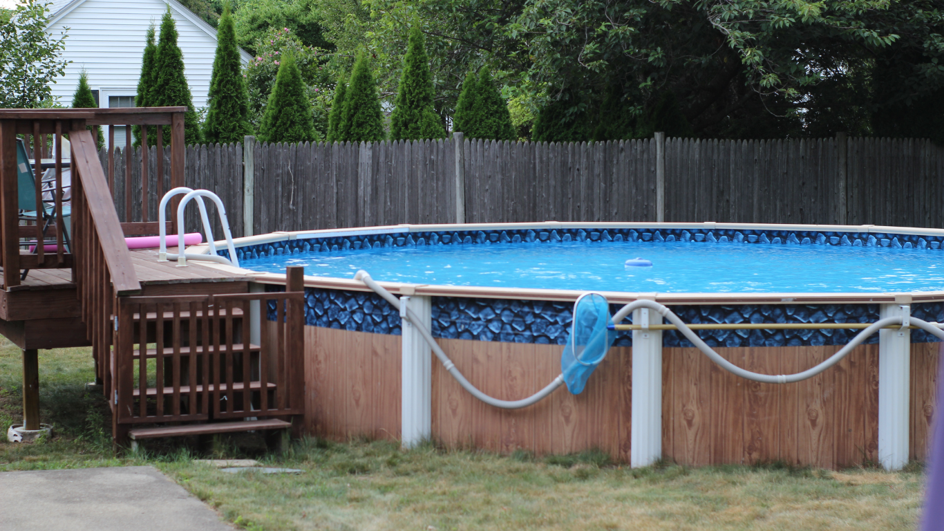Above-ground pool with wooden deck and fence in a backyard setting.