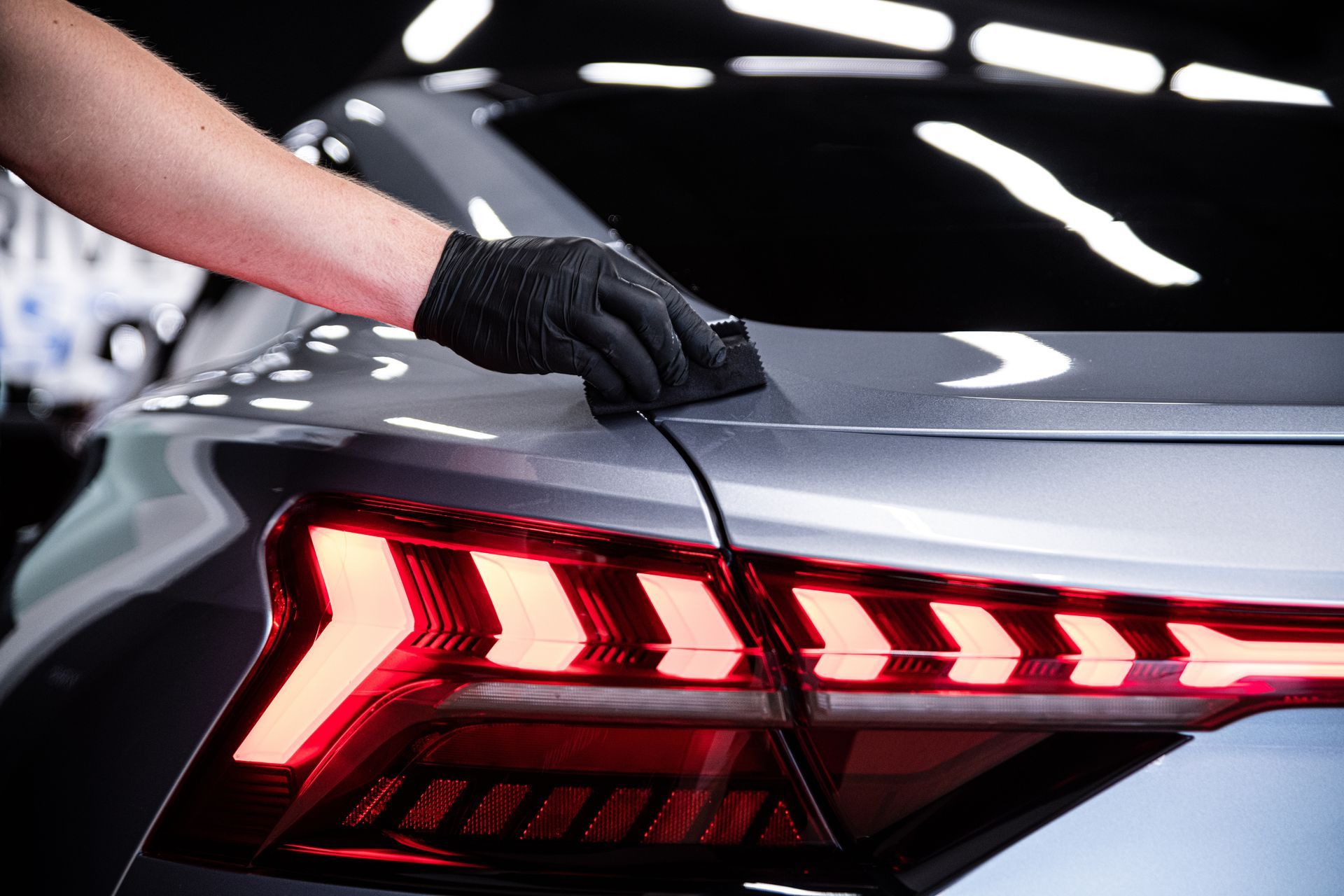 Hand in black glove applying detailing treatment to a gray car near its LED tail light. Hand in black glove applying detailing treatment to a gray car near its LED tail light.