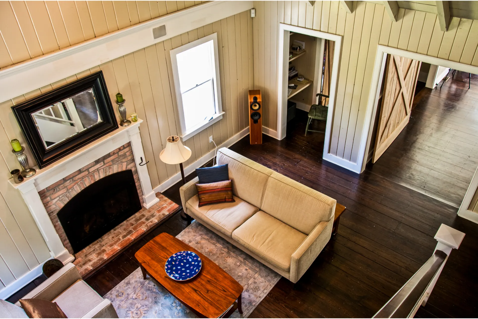 High-angle view of living room with fireplace, sofa, coffee table, and dark wood floor.