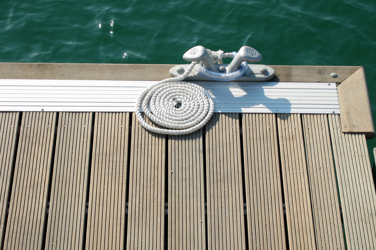 Coiled rope on a wooden dock near a cleat, with water in the background.