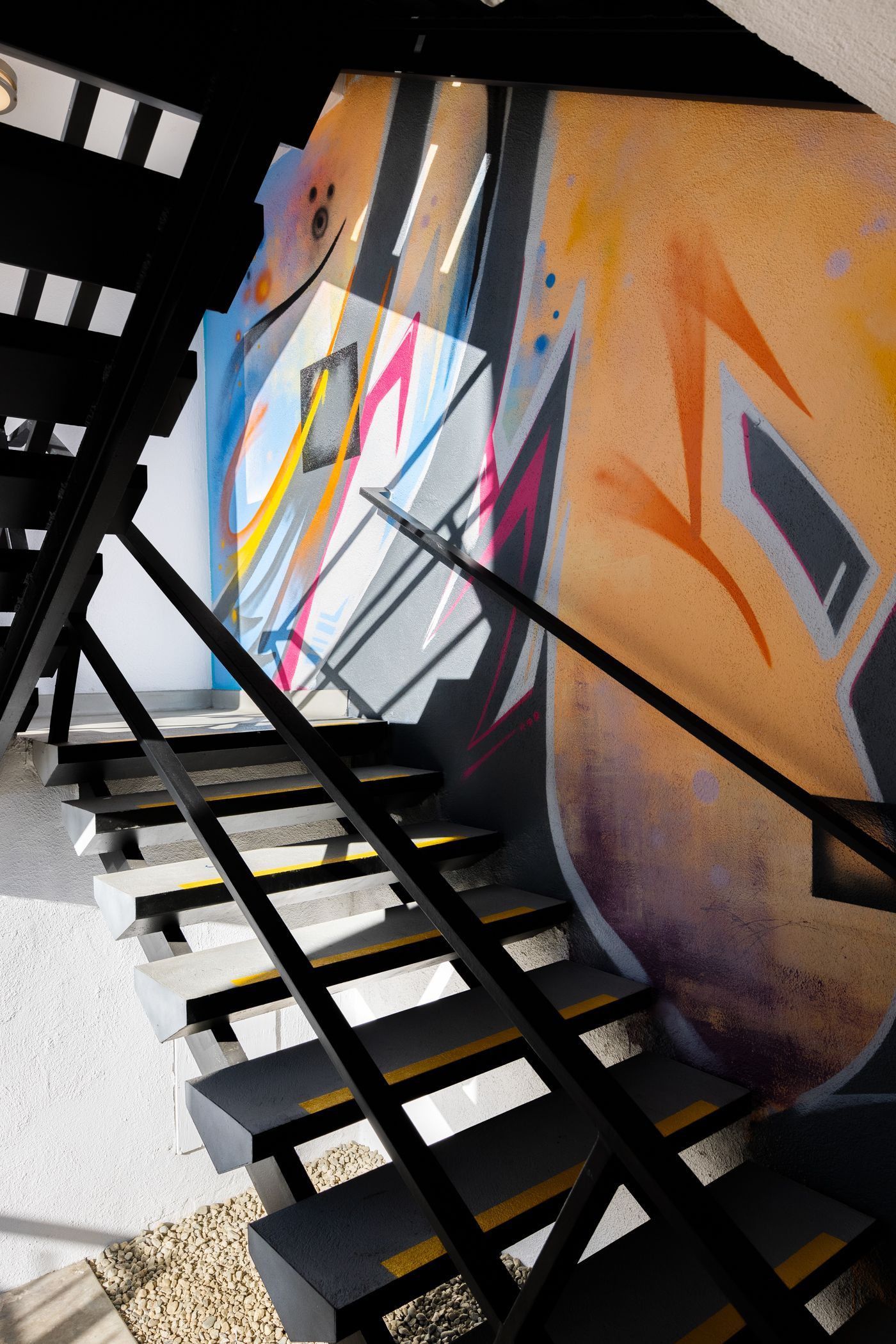 A view looking down a modern staircase with black railings against a wall covered in vibrant, colorful abstract graffiti.