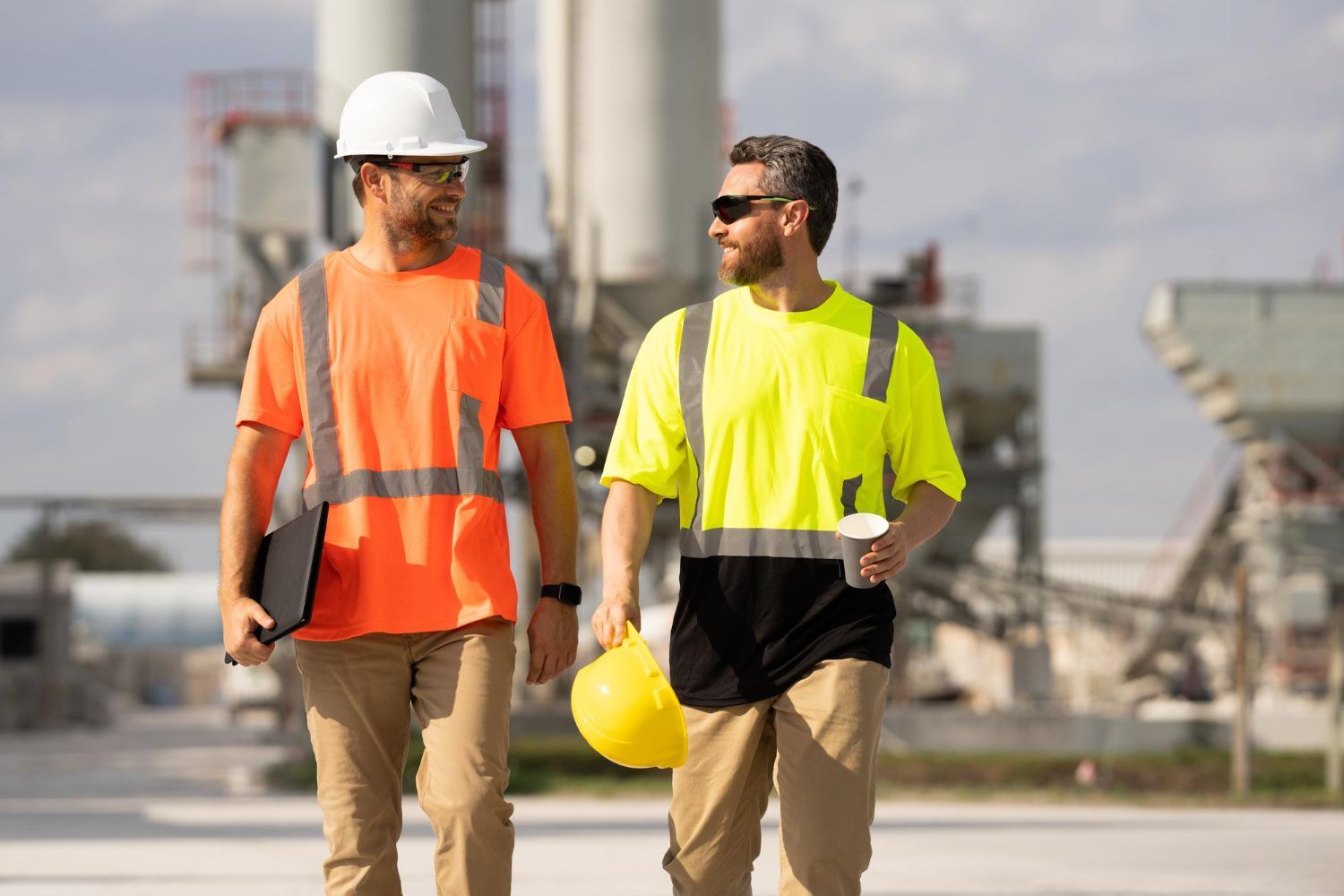 Construction workers in safety gear review blueprints on-site.