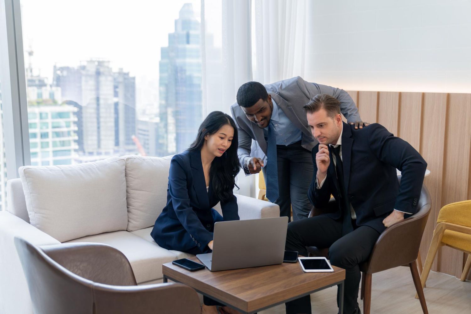 Three business professionals collaborating around a laptop in a modern office, city view.