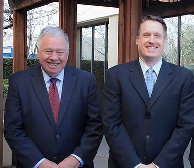 Three businesspeople at a wooden table, reviewing a tablet. Indoor, with plants.