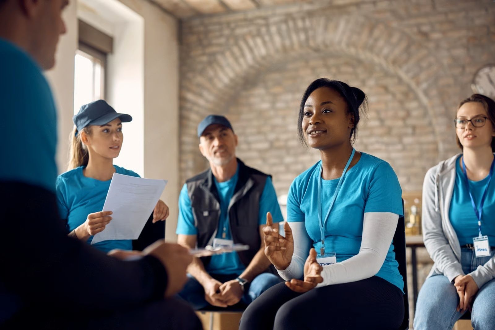 Group of people in blue shirts, in discussion, seated indoors.