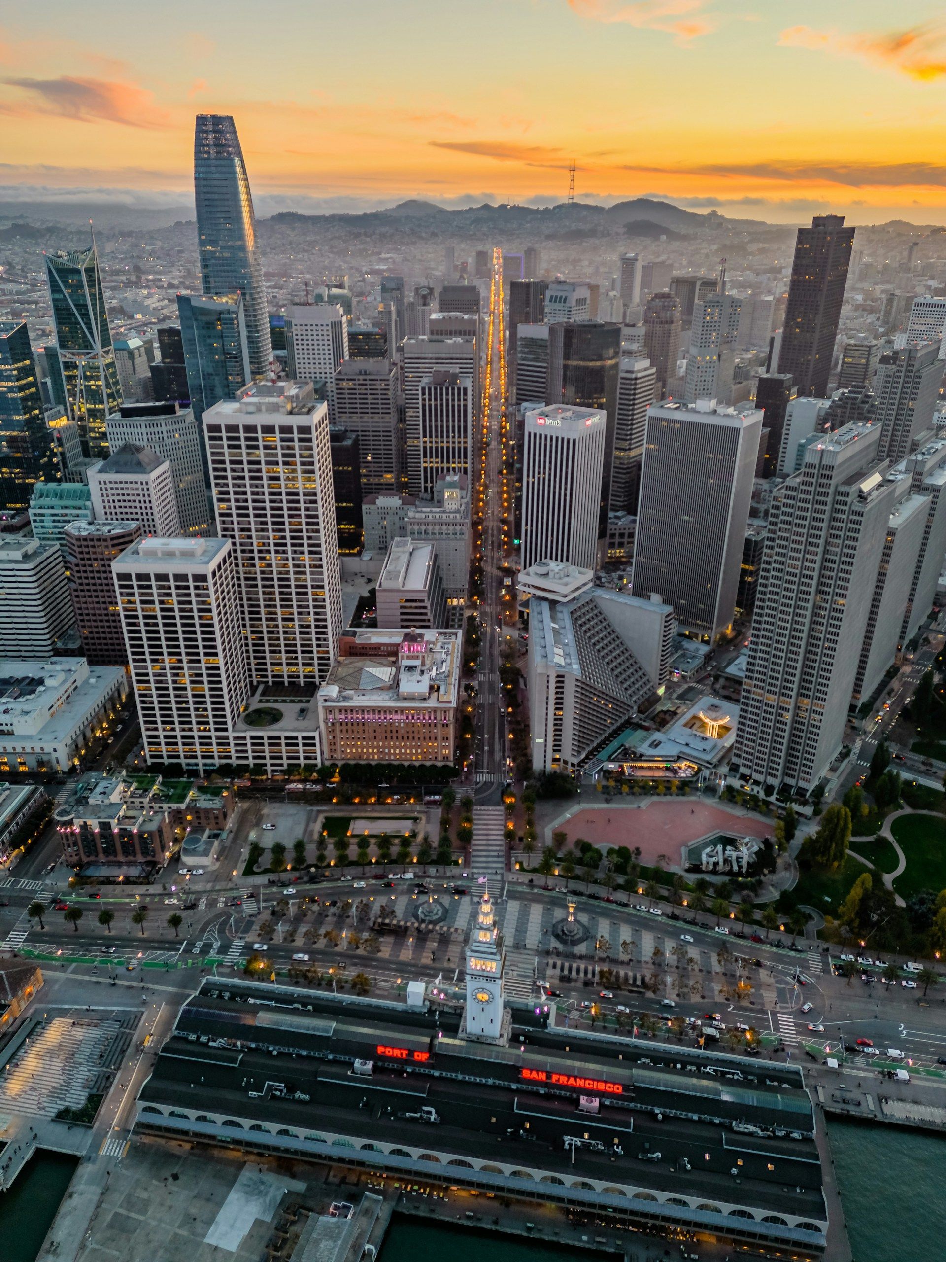 Downtown Los Angeles skyline at dusk with illuminated skyscrapers and palm trees.