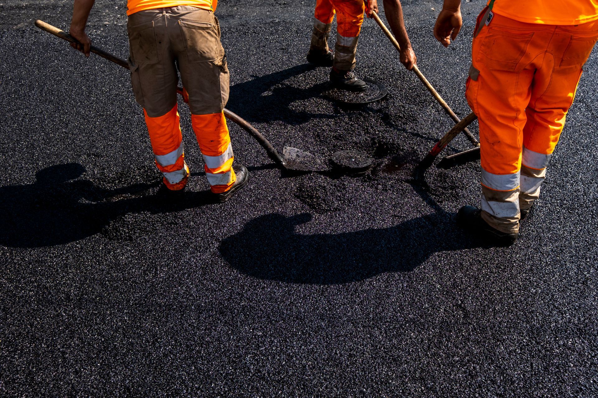 Expert crew providing commercial paving services by hand-leveling fresh asphalt on a parking lot.