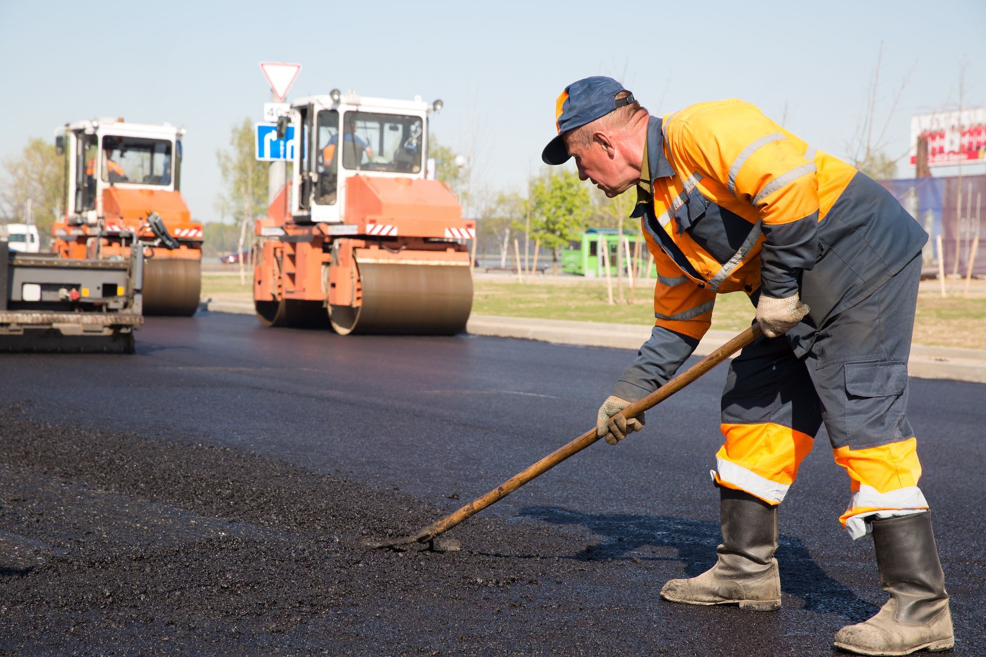 A construction worker during an asphalting of a road. Asphalt machines are near him.