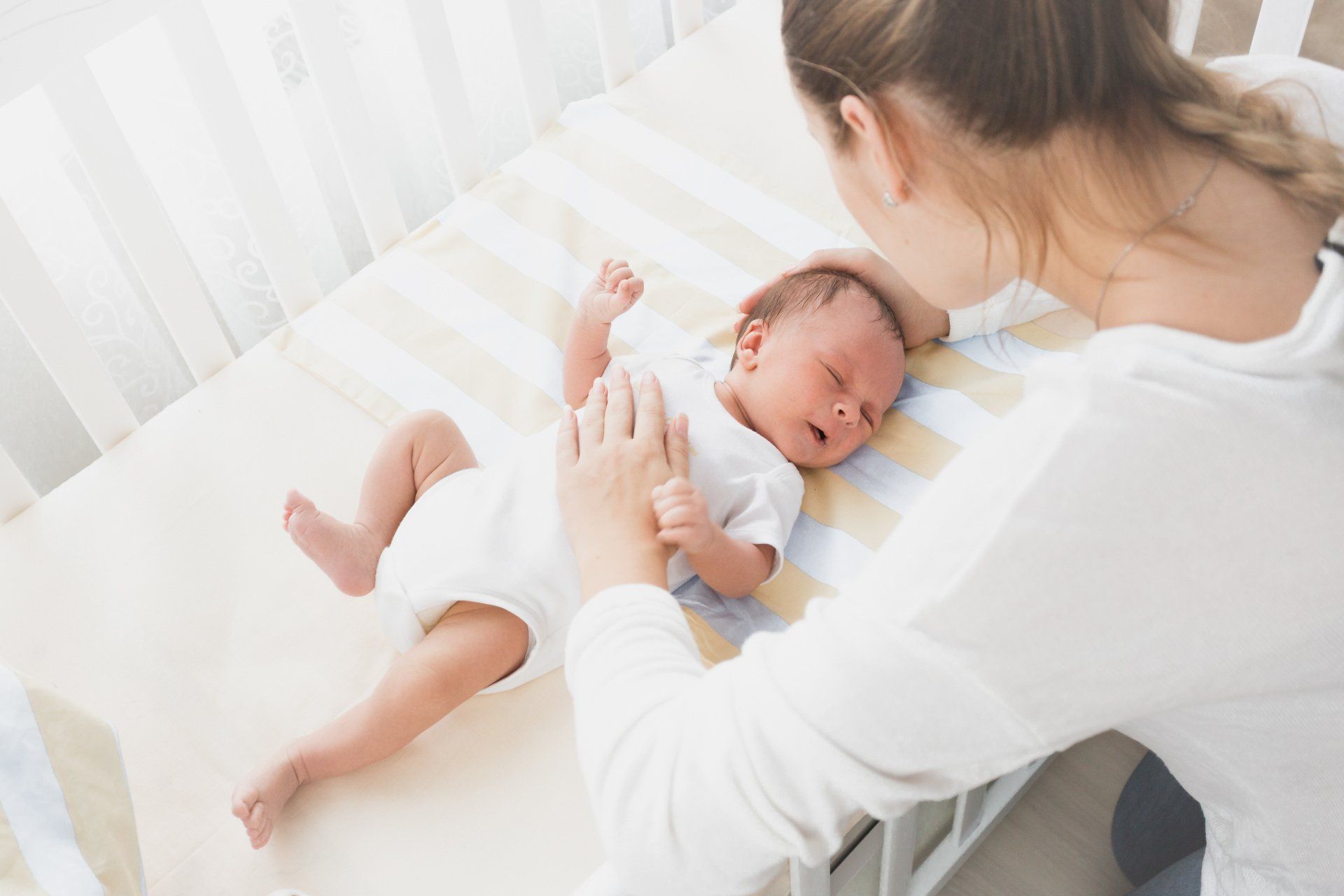mom looking at newborn baby in crib