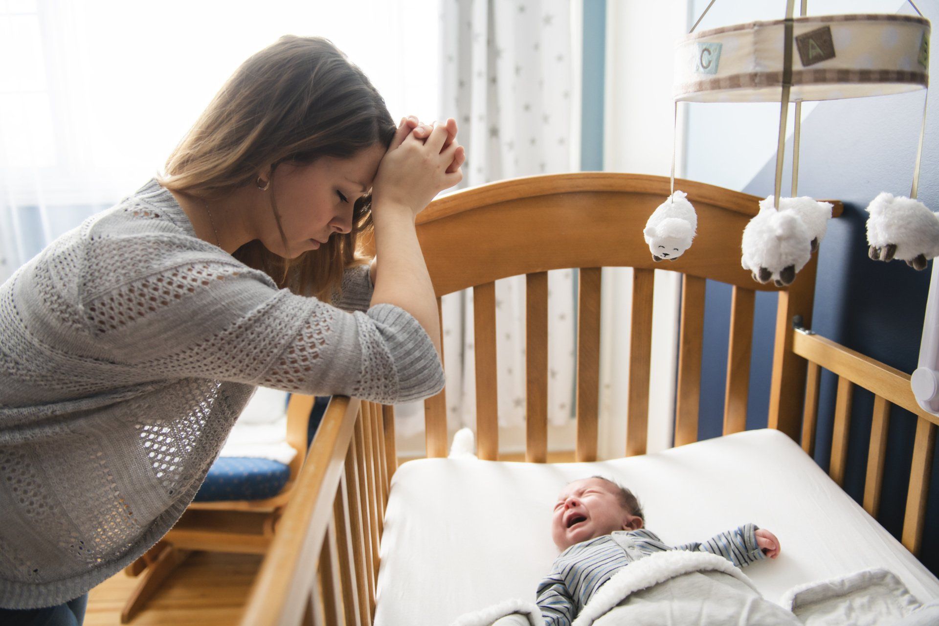 tired mom standing over crib looking at crying baby