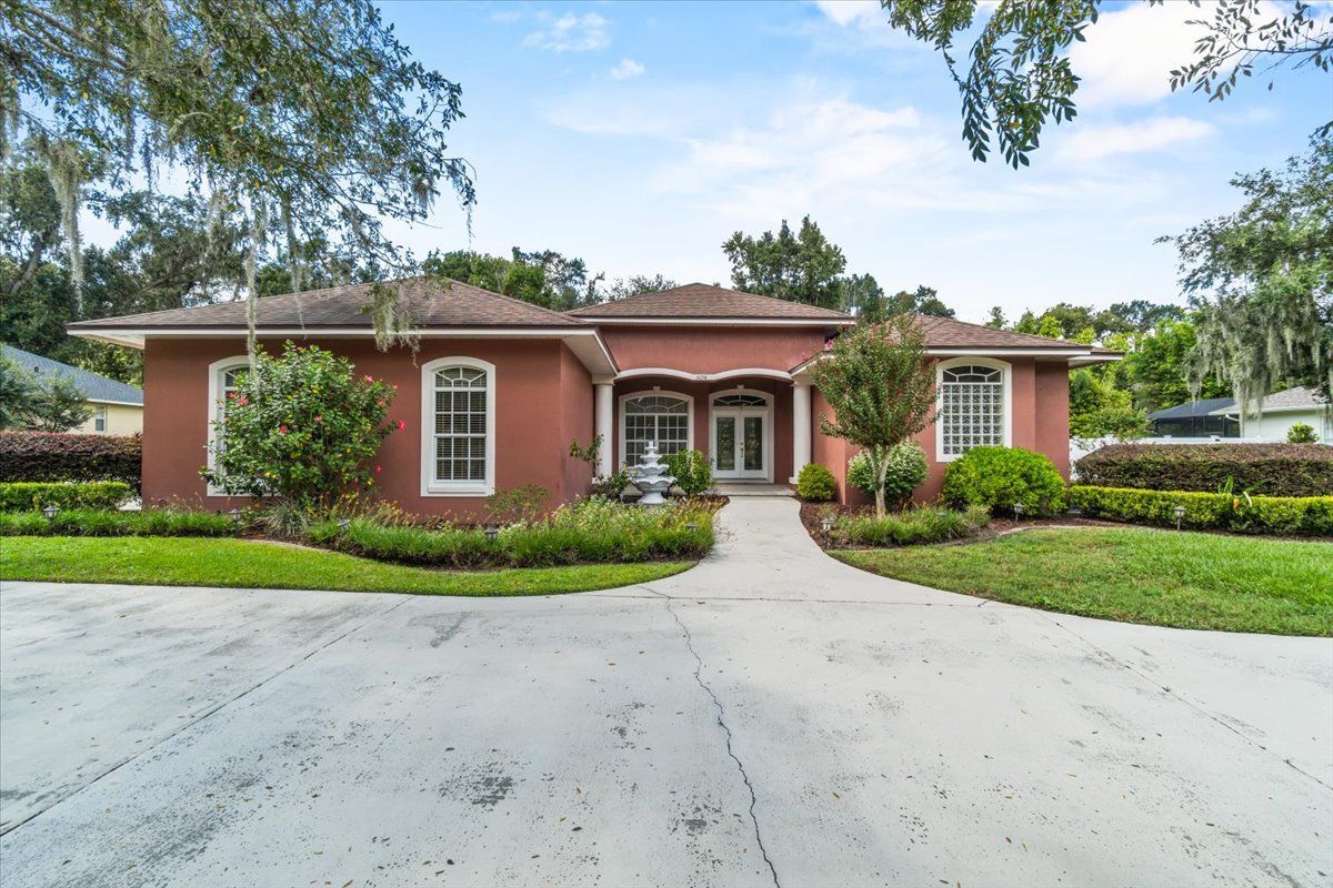Red stucco house with white trim, arched windows, and a paved driveway, surrounded by green landscaping.
