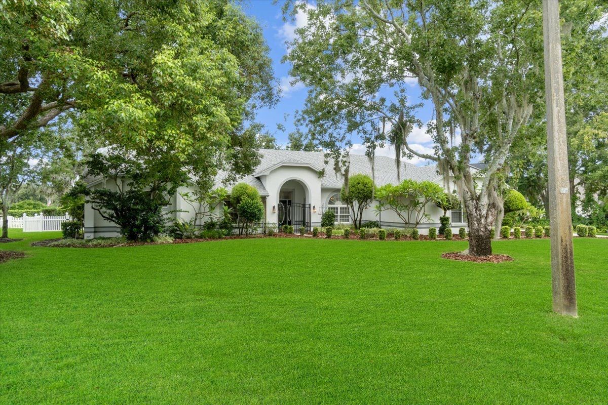 White house with arched entrance and green lawn under a blue sky, trees on each side.