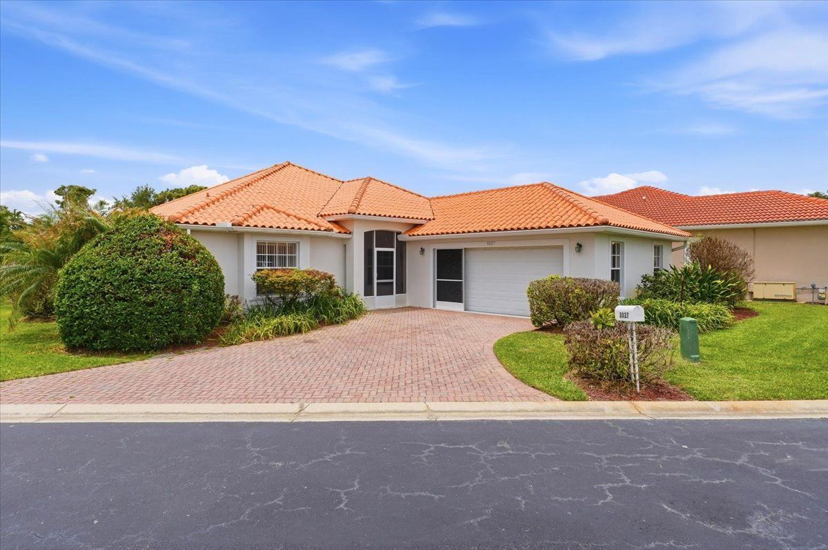 Single-story house with orange tile roof, gravel driveway, and green lawn under a blue sky