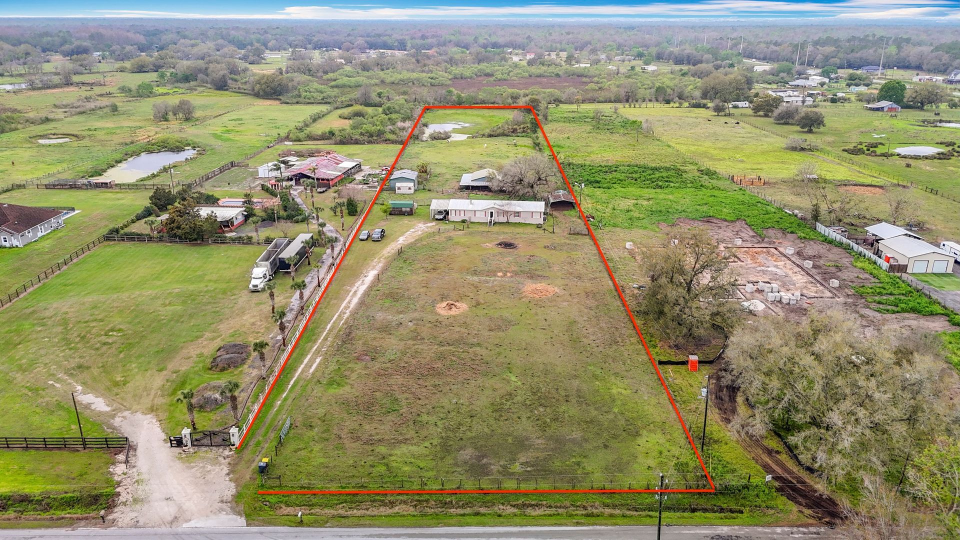 Aerial view of a rectangular grassy plot of land, outlined in red, with a house, and surrounding farmland.