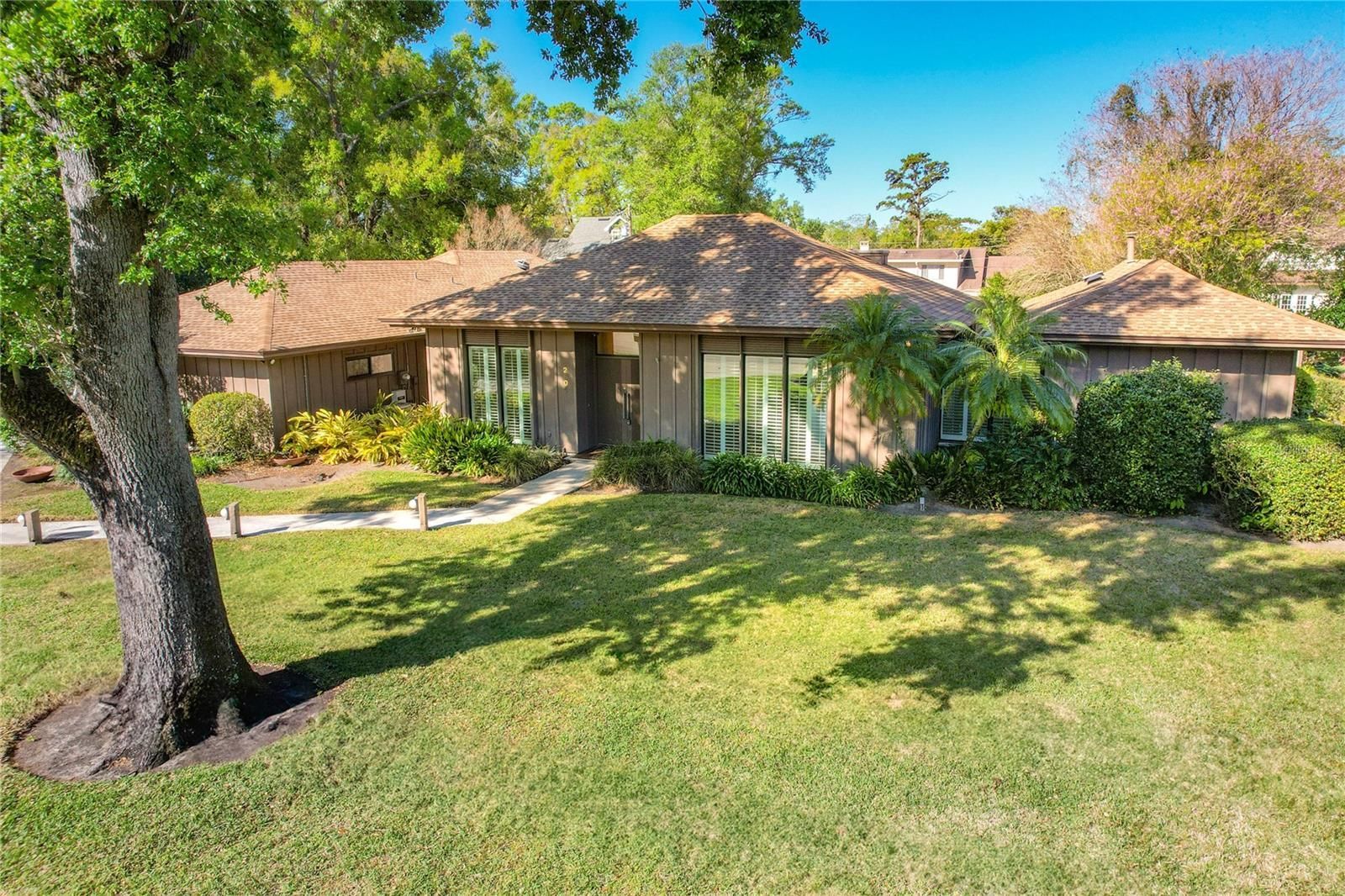 Ranch-style house with brown tiled roof, green lawn, large tree, and landscaping.
