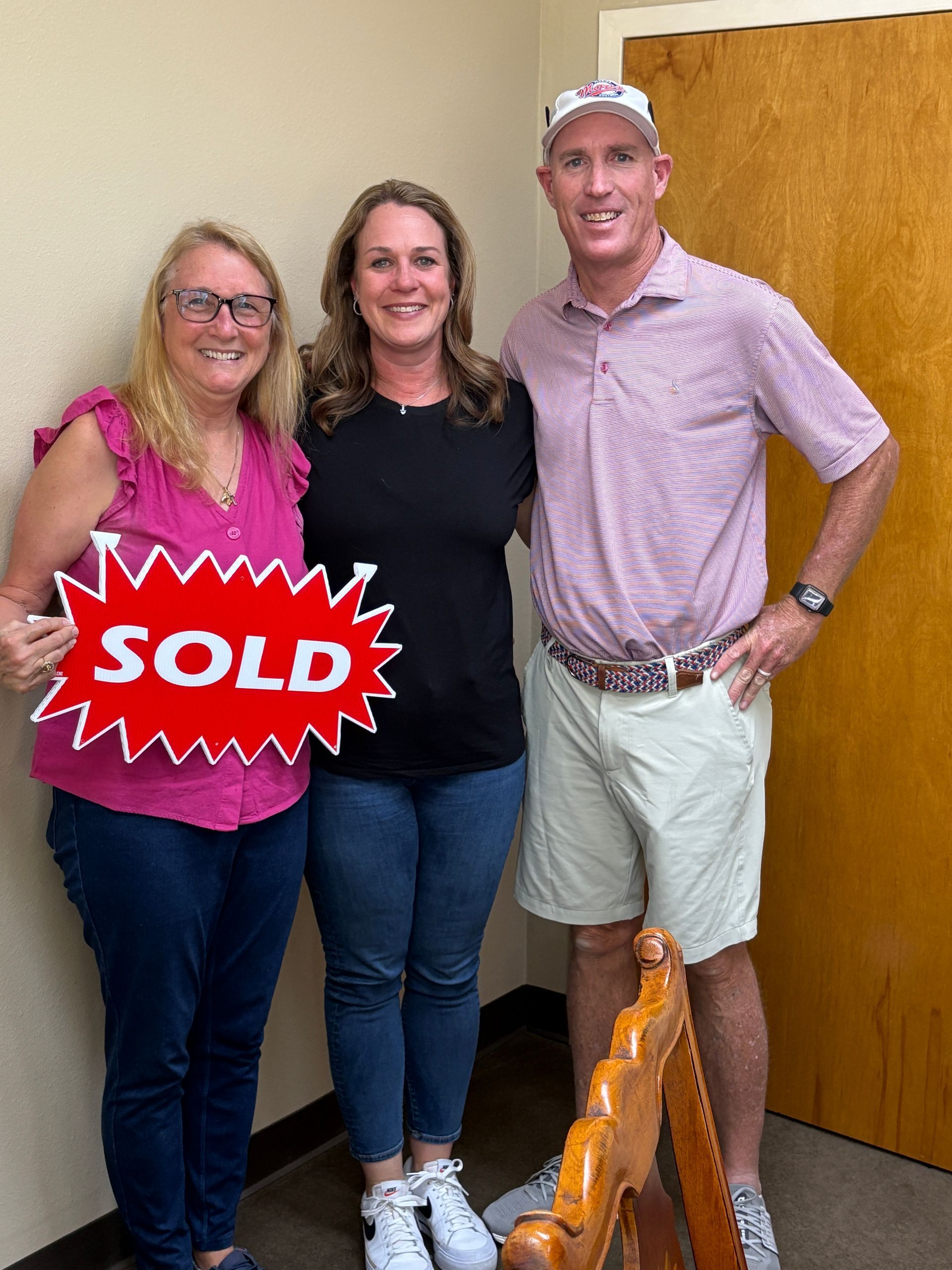 Three people smiling, celebrating a home sale. Woman holding 